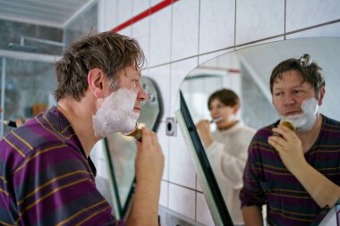 Erkek ve erkek çocuk sabah banyosu yapıyorlar, dişlerini fırçalıyorlar, tıraş oluyorlar ve saçlarını yıkıyorlar.