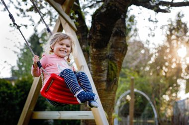 Küçük mutlu kız, salıncakta salıncakta sallanıyor. Güneşli bir bahar gününde ağaçların altında sallanan tatlı sağlıklı bir çocuk. Bebek gülüyor ve ağlıyor.