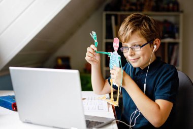 Gözlüklü çocuk evde okulda laptopta öğreniyor. Ev ödevi yapan, defter ve modern aletler kullanan sevimli bir çocuk. Evde eğitim kavramı