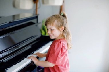 Oturma odasında piyano çalan güzel küçük kız. Sevimli anaokulu çocuğu müzik enstrümanı çalmayı öğrenirken eğleniyor. Çocuklar için erken müzik eğitimi