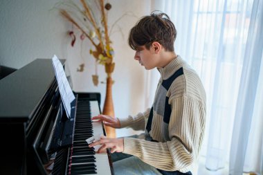 Genç çocuk evde piyano çalıyor. Gençler müzik aletleriyle eğleniyor.