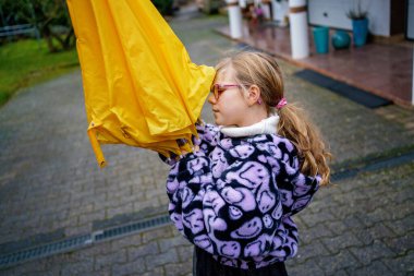 Gülümseyen kız sakin bir sokakta parlak sarı bir şemsiyeyle oynuyor, açık havada çocukluk anıları, neşe, hareket ve günlük hayatı gösteriyor..