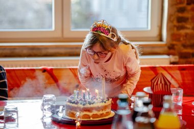 Mutlu çocuk, doğum günü tacı takan küçük liseli kız kapalı bir doğum günü kutlamasında aile ortamında pastaya mum üflüyor..