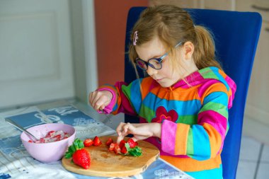 Littl anaokulu bıçak kullanmayı öğreniyor çilek kesmeyi mutfakta kahvaltıda yulaf lapası yapmak için meyve salatası yapmayı. Çocuklar için sağlıklı yiyecekler