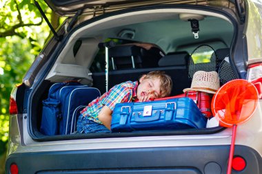 Yaz tatilinden önce ailesiyle birlikte araba bagajında oturan sevimli küçük çocuk. Bavulları ve oyuncakları olan mutlu çocuk seyahate çıkıyor, gerçek hayat, gerçek insanlar..