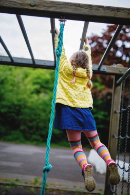 Küçük kız tırmanma iskeletinde jimnastik yapıyor, okul bahçesinde yatay bar. Çocuk okul tatilinde eğleniyor