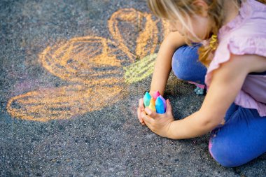 Dışarıda oynarken kaldırımda tebeşir tutan küçük kız, yukarıdan çekilmiş yaratıcı çocukluk anı, gerçek insanlar..