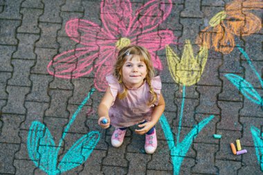 Yürümeye başlayan kız, kaldırım tebeşiri ile renkli çiçekler çiziyor, kaldırımda yaratıcı bir oyun oynuyor, tasasız bir çocukluk geçiriyor, gerçek insanlar.