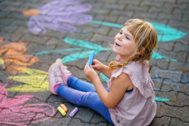 Yürümeye başlayan kız, kaldırım tebeşiri ile renkli çiçekler çiziyor, kaldırımda yaratıcı bir oyun oynuyor, tasasız bir çocukluk geçiriyor, gerçek insanlar.