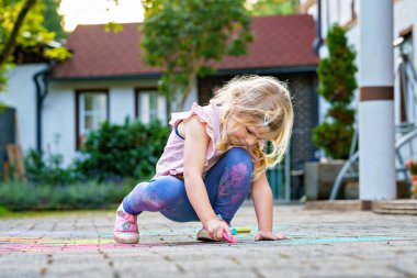 Evinin önündeki kaldırıma renkli tebeşirler çizen genç bir kız, yaratıcı açık hava oyunları, gerçek hayatta çocukluk yaratıcılığı, gerçek insanlar. Küçük çocuk eğleniyor..