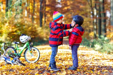 İki küçük çocuk, sonbahar ormanında en iyi arkadaşlar. Ağabeyim, doğada güneşli bir sonbahar gününde bisiklete binmeden önce küçük çocuğun kaskını takmasına yardım ediyor. Güvenlik, spor, çocuk konseptiyle eğlence..