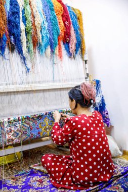 Buhara, Özbekistan - 29 Mart 2024: Buhara, Özbekistan 'da geleneksel bir dokuma tezgahında renkli yün iplikleri ve antik zanaat teknikleriyle el yapımı bir halı örücüsü.
