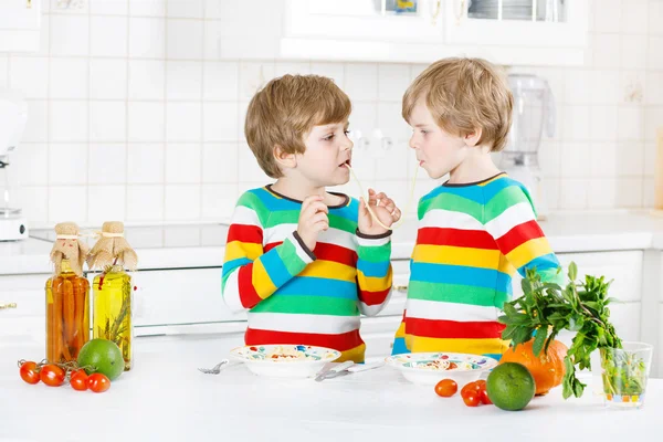 Dvě malé dítě chlapce jíst špagety v domácí kuchyni. — Stock fotografie