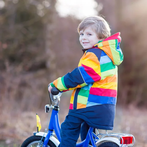 Kid boy in safety helmet and colorful raincoat riding bike, outd — Stock Photo, Image