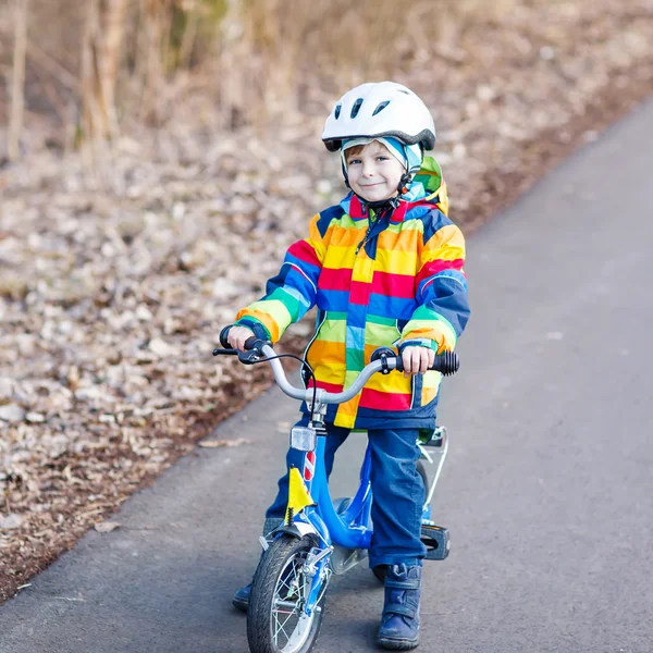 Niño en casco de seguridad y colorido impermeable bicicleta de montar, outd — Foto de Stock