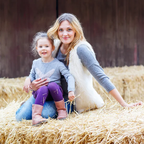 Menina feliz e mãe se divertindo com feno em uma fazenda — Fotografia de Stock