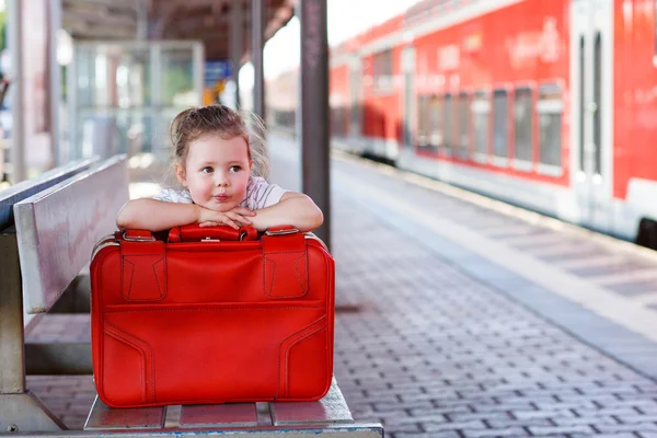 Niña con una gran maleta roja en una estación de tren — Foto de Stock