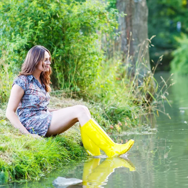 Joven hermosa mujer sentada en barcos de goma de lluvia amarilla por un r — Foto de Stock