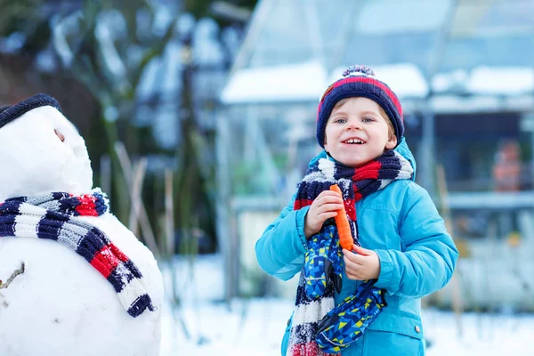 Lustiger Junge, der im Winter draußen einen Schneemann bastelt — Stockfoto