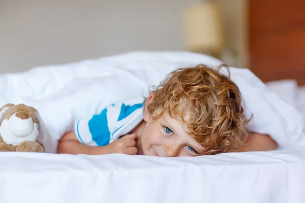 Schattig kind jongen na het slapen in zijn witte bed met speelgoed — Stockfoto