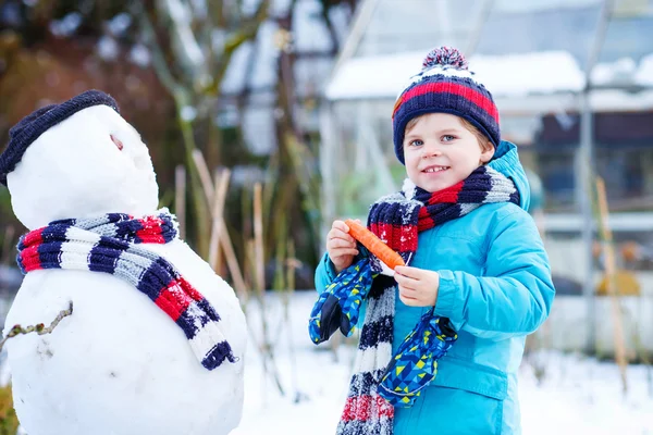 Little kid boy making a snowman in winter — Stock Photo, Image