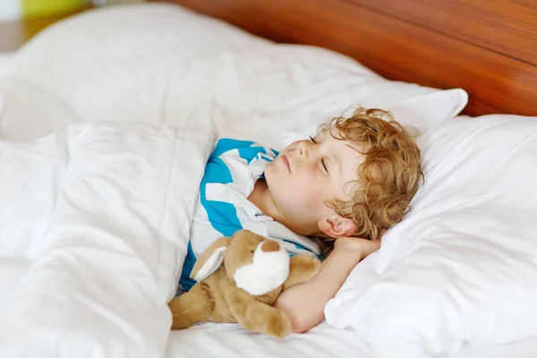 Μικρό ξανθό παιδί που κοιμάται στο κρεβάτι του με το παιχνίδι. — Φωτογραφία Αρχείου