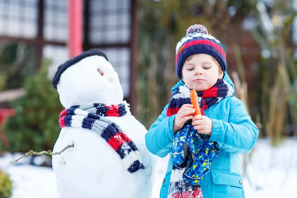 Funny kid boy making a snowman in winter outdoors — Stock Photo, Image