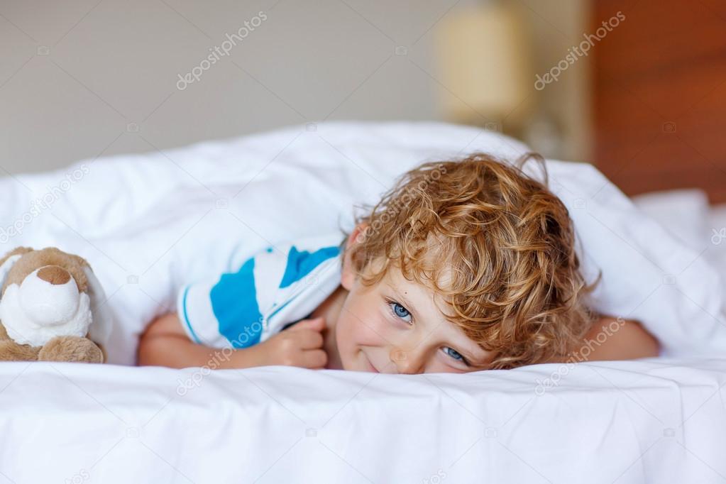 Adorable kid boy after sleeping in his white bed with toy