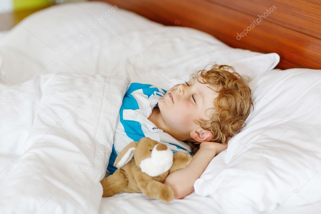 Little blond child sleeping in his bed with toy.