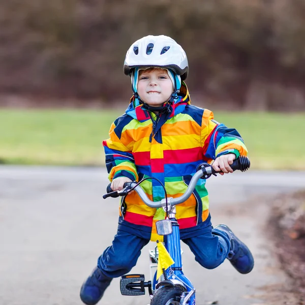 Engraçado menino pré-escolar bonito em capacete de segurança e capa de chuva colorida montando sua primeira bicicleta — Fotografia de Stock