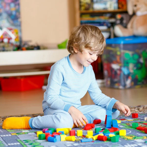 Piccolo bambino biondo che gioca con blocchi di legno colorati al coperto — Foto Stock