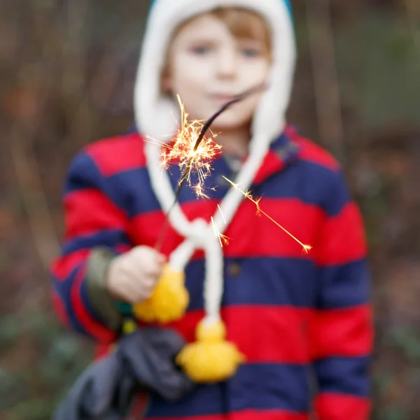 Little child in winter clothes holding burning sparkler — Zdjęcie stockowe