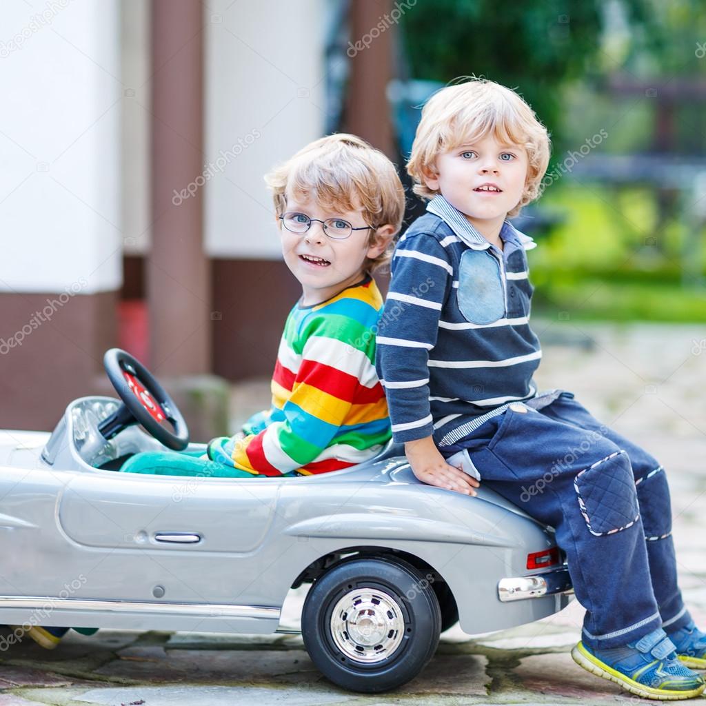 Two happy kids playing with big old toy car in summer garden, ou