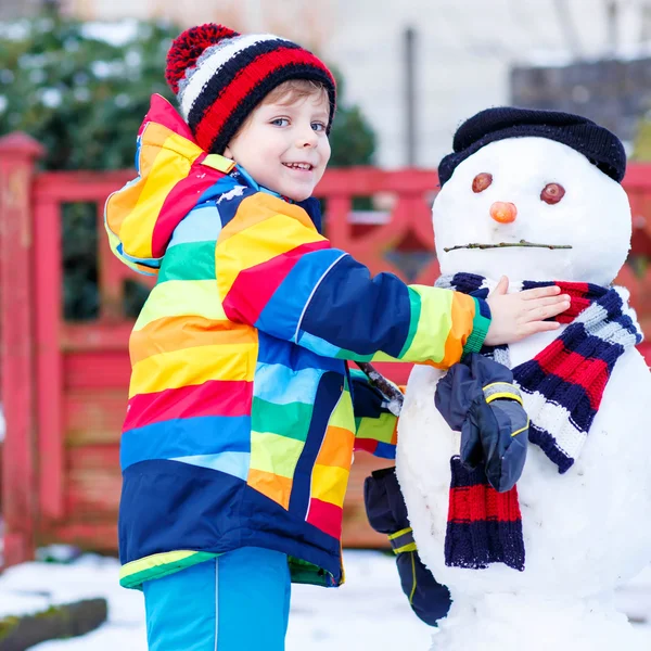 Funny kid boy att göra en snögubbe på vintern — Stockfoto