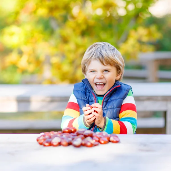 Liten blond unge leker med kastanjer i höst park. — Stockfoto