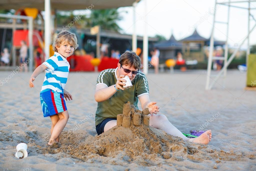 Happy father and and little son building sand castle on sand bea