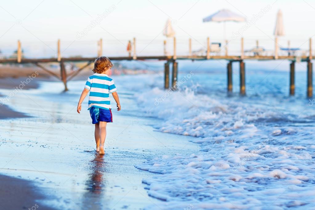 Happy little kid boy having fun with running through water in oc