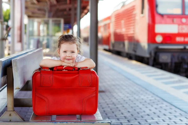 Niña con una gran maleta roja en una estación de tren — Foto de Stock