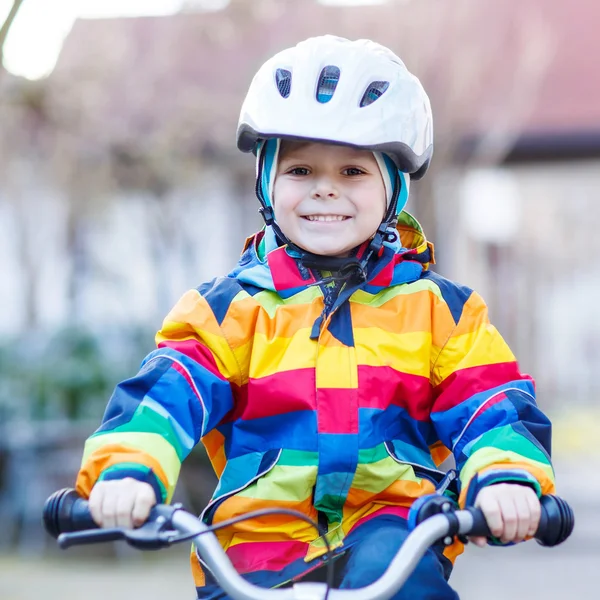 Kid boy in safety helmet and colorful raincoat riding bike, outd — Stock Photo, Image