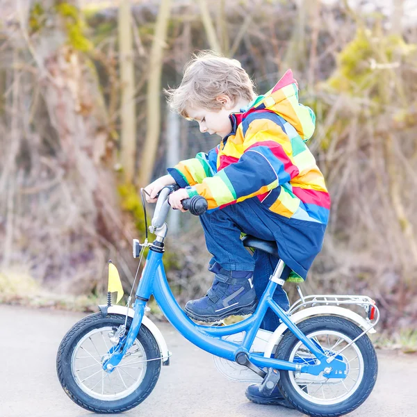 Kid boy in safety helmet and colorful raincoat riding bike, outd — Stock Photo, Image