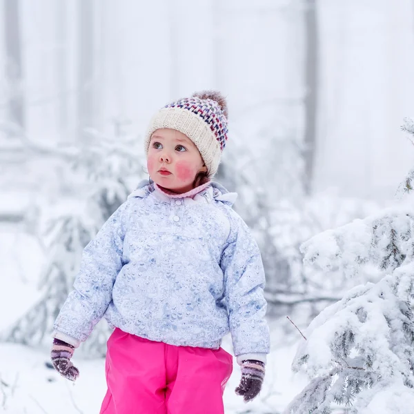 Portrait of a little girl in winter hat in snow forest at snowfl — ストック写真