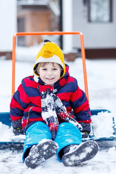 Funny kid boy har roligt med ridning på snöskyffel, utomhus — Stockfoto