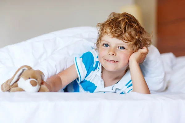 Adorable kid boy after sleeping in his white bed with toy — Stock Photo, Image