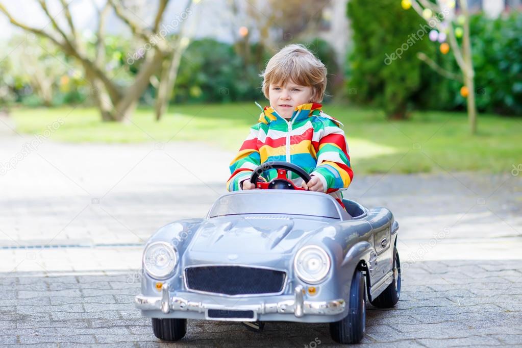 Little preschool boy driving big toy old vintage car, outdoors