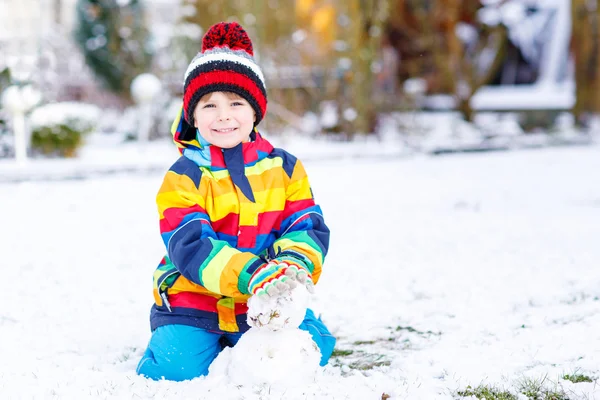 Beautiful kid boy in colorful clothes making a snowman — Stock Photo, Image