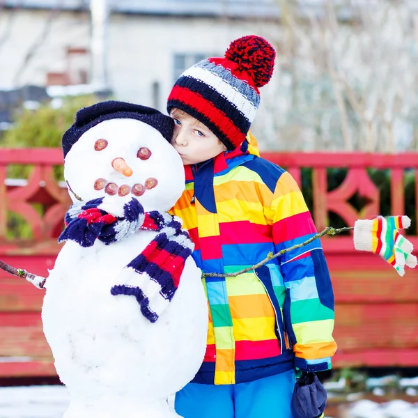 Funny kid boy making a snowman in winter — Stock Photo, Image