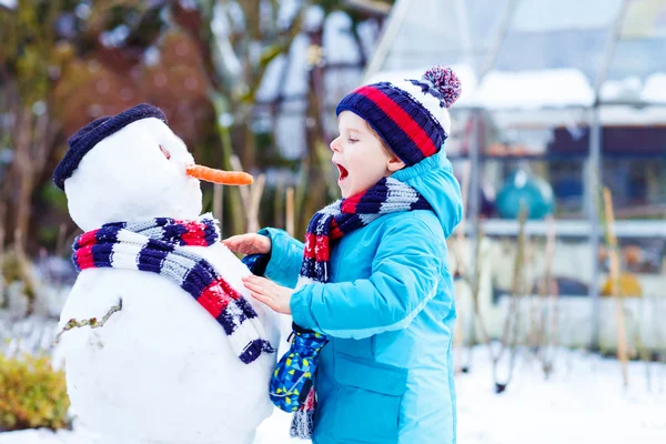 Lustige Junge in bunten Kleidern, die einen Schneemann, im Freien — Stockfoto