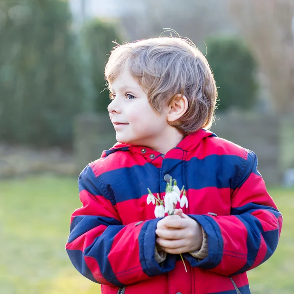 スノー ドロップの花を持って赤のジャケットの少年をキッドします。 — ストック写真