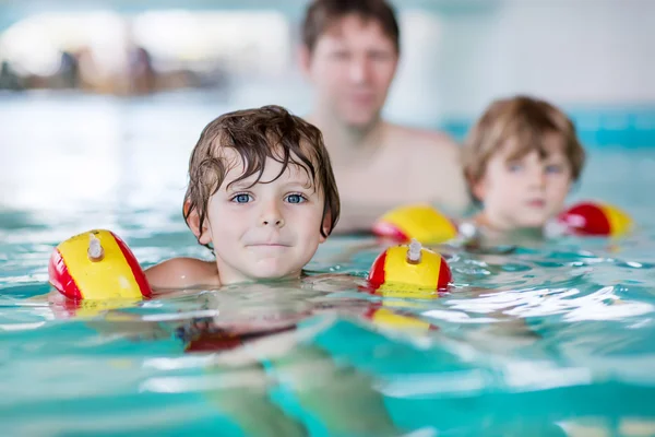 Nuori isä opettaa kahta pientä poikaansa uimaan sisätiloissa. — kuvapankkivalokuva
