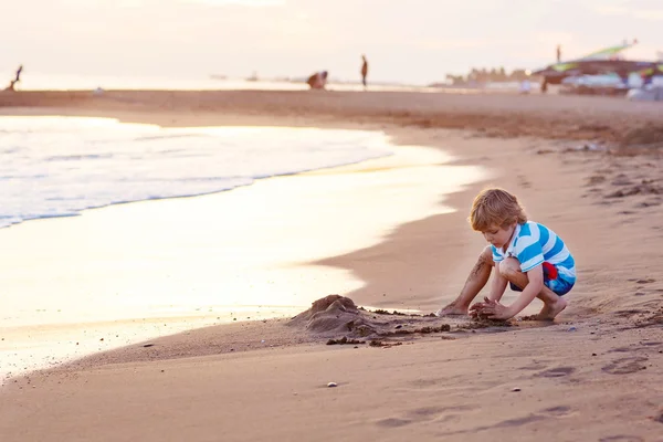 Menino pequeno feliz se divertindo com castelo de areia pelo oceano — Fotografia de Stock